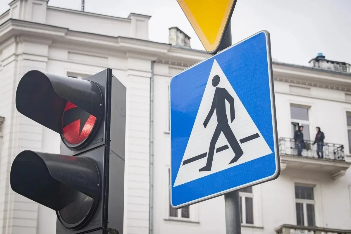Pedestrian crossing sign and red traffic light against a pale building facade